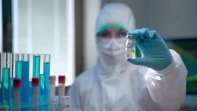 专业女性病毒学家手中的疫苗小瓶特写镜头穿着防护服，自信的实验室工作人员在成功的化学实验和困难的化学分