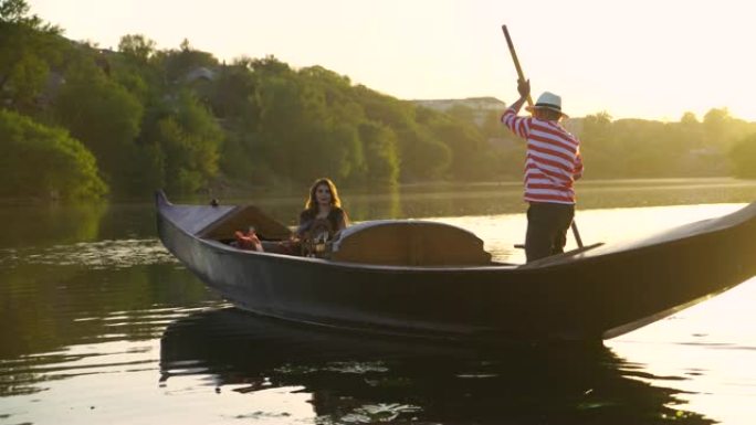 美丽的女人坐在船上，一个男人在日落时在自然背景上划船。