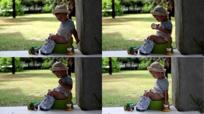 可爱的蹒跚学步的男孩，坐在度假胜地露台后门廊的便盆上，玩玩具