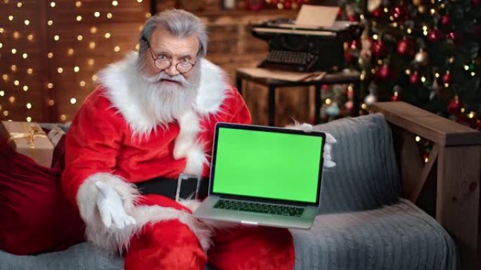 友好的男性圣诞老人拿着笔记本电脑绿屏吸引眼球。用4K红色相机拍摄