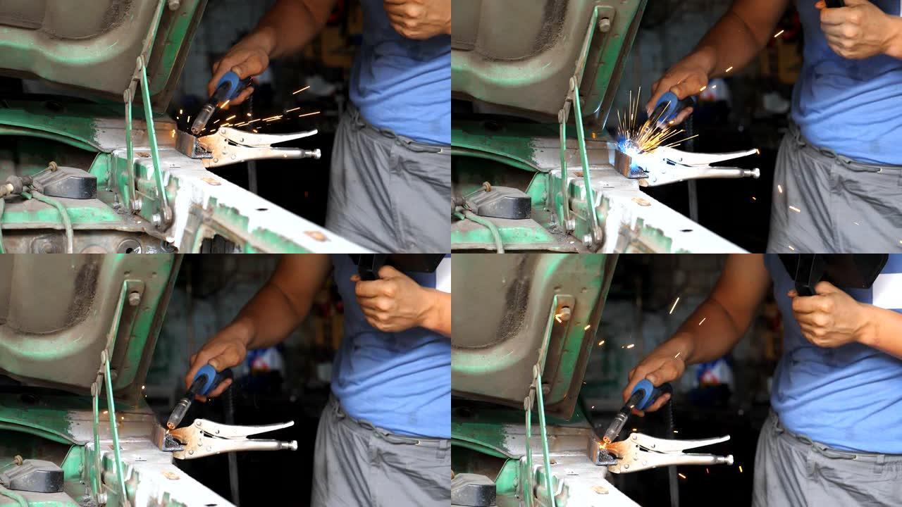 成人汽车制造商的男性手在车库用焊接机焊接旧车的金属零件。修理工或机械工人的手臂在车间使用专业设备进行