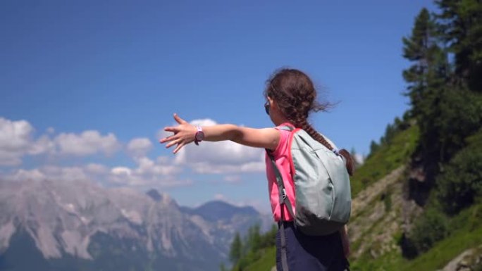 女孩在奥地利阿尔卑斯山美丽的夏日徒步旅行，在岩石上休息，欣赏山峰的壮丽景色。带着孩子积极的家庭度假休