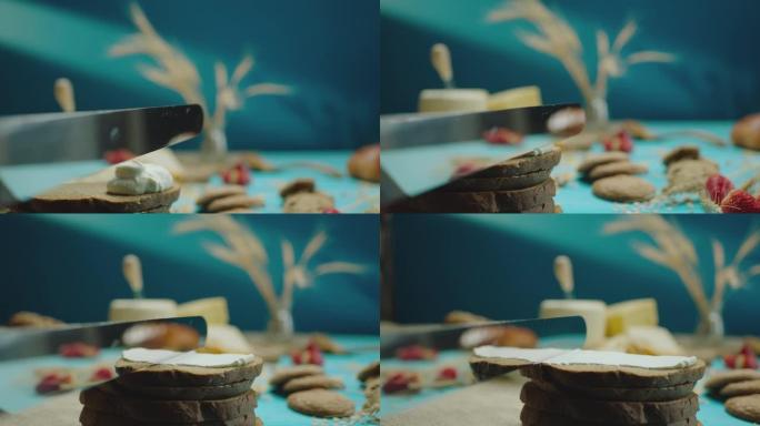 特写柔和的黄油或酸奶油在蓝色背景的桌子上用金属刀在乡村黑麦面包上慢动作。特写制作酸奶油三明治。用相机