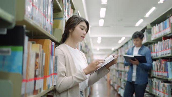 聪明的亚洲男女大学生在校园图书馆书架之间看书，有复印空间。