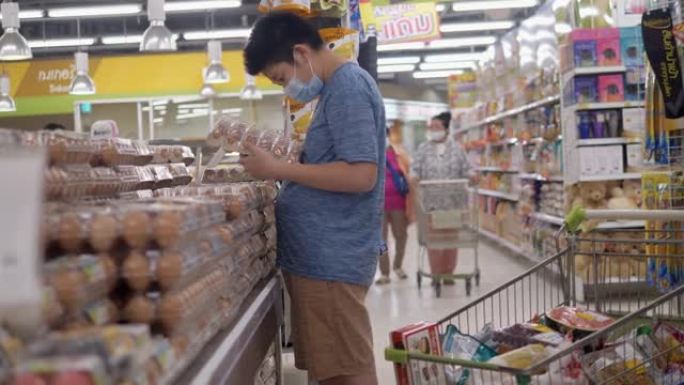 亚洲男孩戴着口罩，在新型冠状病毒肺炎前为家人囤积食物，生活方式概念。
