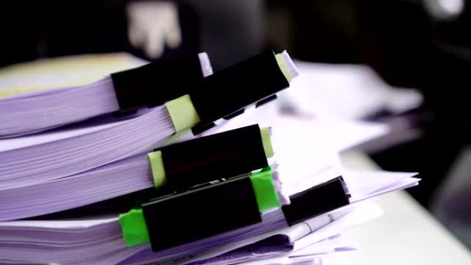 一堆未完成的文件将文书工作和报告文件堆叠在繁忙的工作过度的桌子上，模糊的商人手在搜索信息。企业与会计