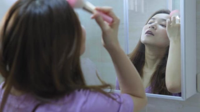 美丽的亚洲女人在镜子前化妆
