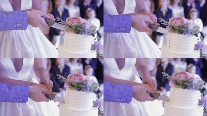 新娘和新郎正在切他们的结婚蛋糕。手切一块蛋糕