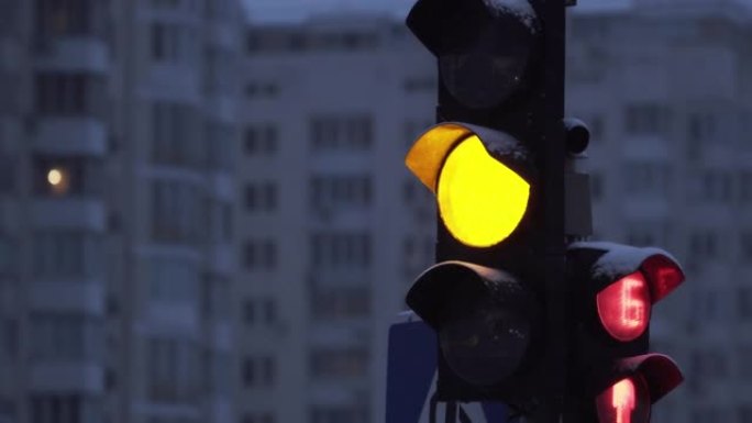 降雪时，傍晚城市街道上的交通信号灯。特写。冬季建筑物背景上的交通信号灯