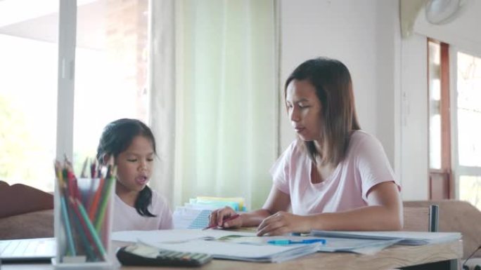 亚洲女学生在做作业，而母亲在家工作。母亲教女儿做作业，由于Covid 19大流行，他们在检疫期间呆在