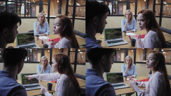 相机向下倾斜女程序员在笔记本电脑屏幕上讨论代码并坐在办公室里的女人附近时与男同事打手势和交谈