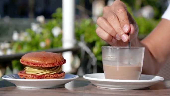 一杯热巧克力和一个橙色蛋糕。这个女人正在法国的一个露台上用勺子搅拌热巧克力。