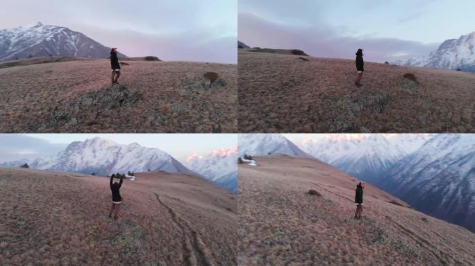 Arial view穿着时髦的滑雪服装，戴着帽子的女孩站在日落后的一个高山夜晚，欣赏山脉的景色。