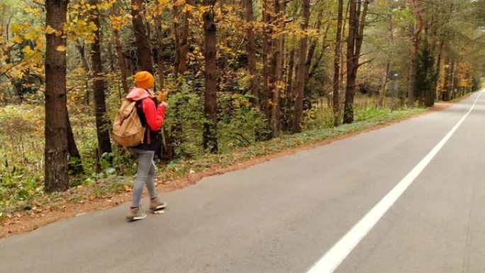 一个戴着黄色帽子和老式背包的年轻苗条女孩沿着柏油路走