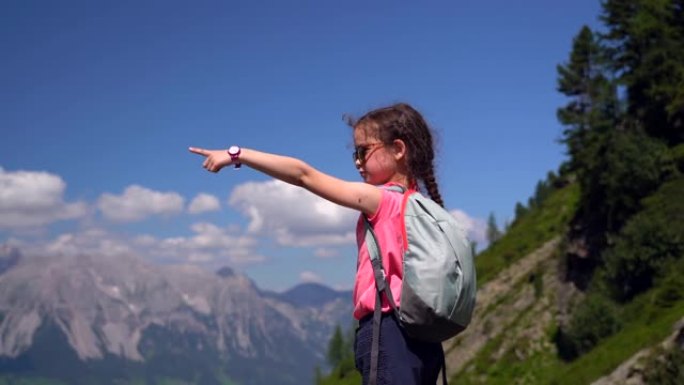 女孩在奥地利阿尔卑斯山美丽的夏日徒步旅行，在岩石上休息，欣赏山峰的壮丽景色。带着孩子积极的家庭度假休