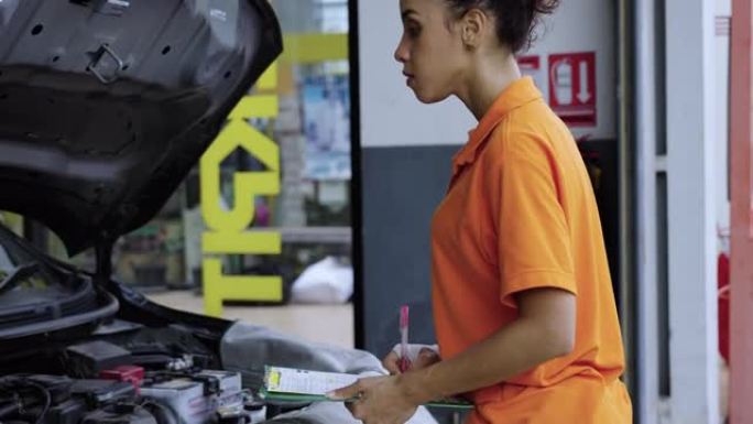 穿着橙色制服的女机械师在汽车服务站工作。专业技工在汽车维修车库工作。