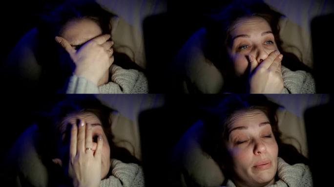 深夜，美丽的昏昏欲睡的女人躺在黑暗房间的沙发上，手里拿着智能手机