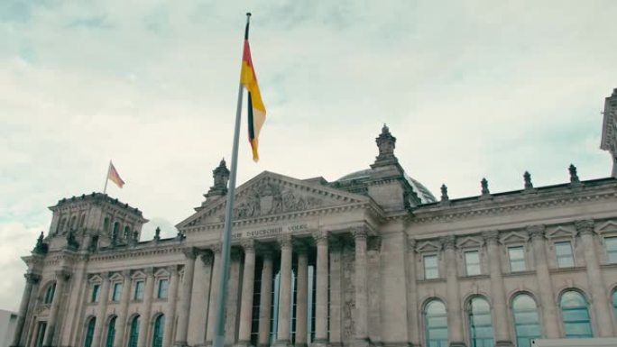 慢动作德国国旗在首都柏林市中心联邦议院议会大楼中央入口的背景下。在蓝色宁静的天空背景下。议会制与政治
