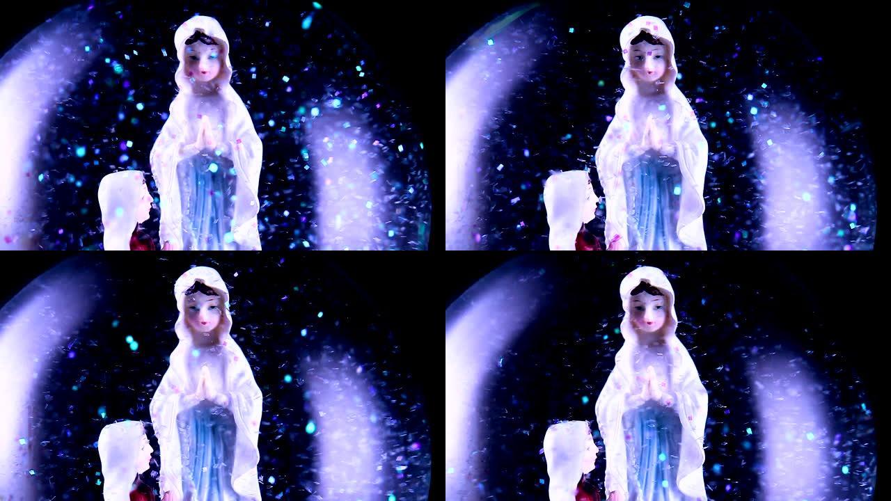 圣母玛利亚和一个信徒跪在雪球里的特写镜头。背景完全是黑色的。雪球里有很多闪闪发光的闪光。