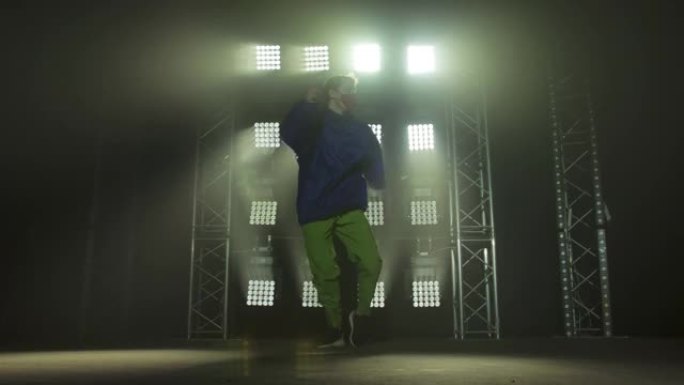才华横溢的年轻嘻哈舞者的剪影。嘻哈街舞在黑暗工作室的舞台上，有烟雾和霓虹灯。动态照明效果。创造技能。