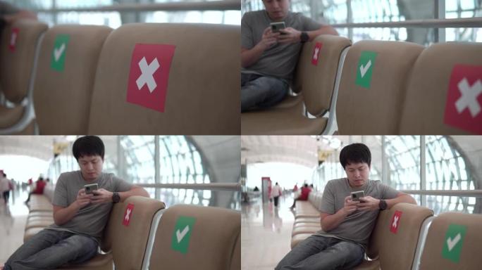 亚洲男子在机场使用智能手机坐在新空间社交距离等待。