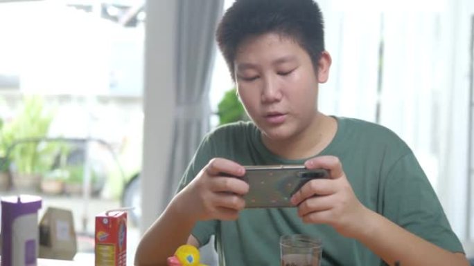 快乐的亚洲男孩在家里靠窗玩智能手机在线游戏，女孩在户外蹦床跳跃，生活方式概念。