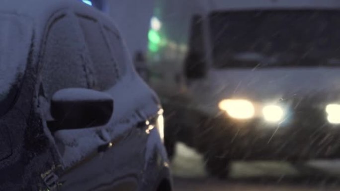 夜间降雪期间，汽车沿着积雪覆盖的城市道路行驶。高速公路上发生事故的危险。旋风期间的艰难路况