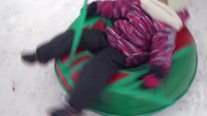 这个女孩正在雪地里的充气戒指上旋转。一个穿着暖和衣服的女孩躺在充气戒指上，用绳子解开