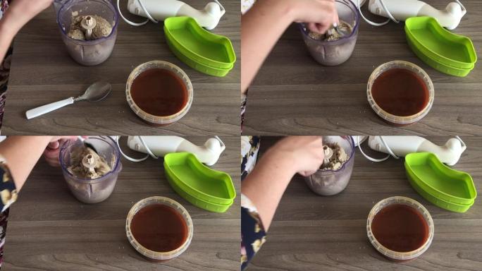 一名妇女取下搅拌机的盖子，用勺子切碎的花生和种子混合，制成halva。容器旁边是蜂蜜，可以添加到混合
