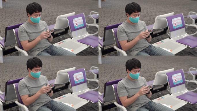 亚洲男子戴着防护口罩，在机场使用智能手机坐在新空间社交距离。