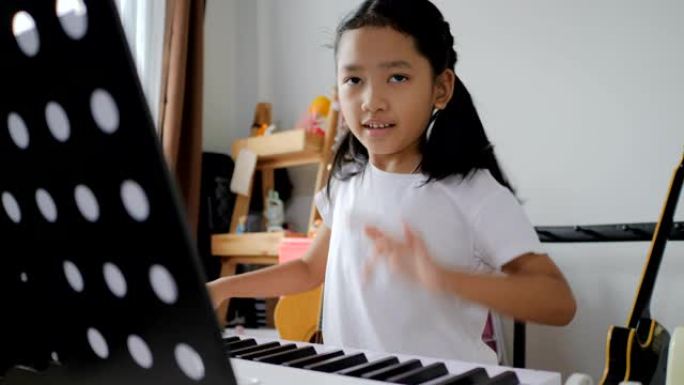 亚洲小女孩在家学习使用电子合成器键盘弹奏基础钢琴