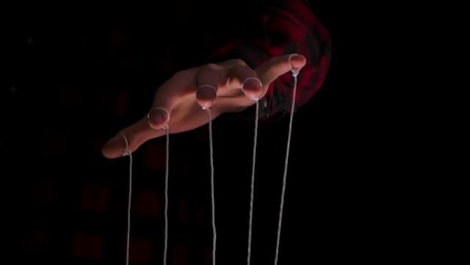 拿着木偶绳子的人。在黑色背景上，近距离的人手控制着一个带有手指的木偶。控制概念。慢动作