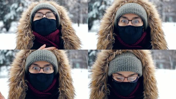 一个戴着绿色帽子和蓬松兜帽的迷人女人，遵守个人保护规则，走在白雪覆盖的公园里。浪漫的年轻幸福的女人走