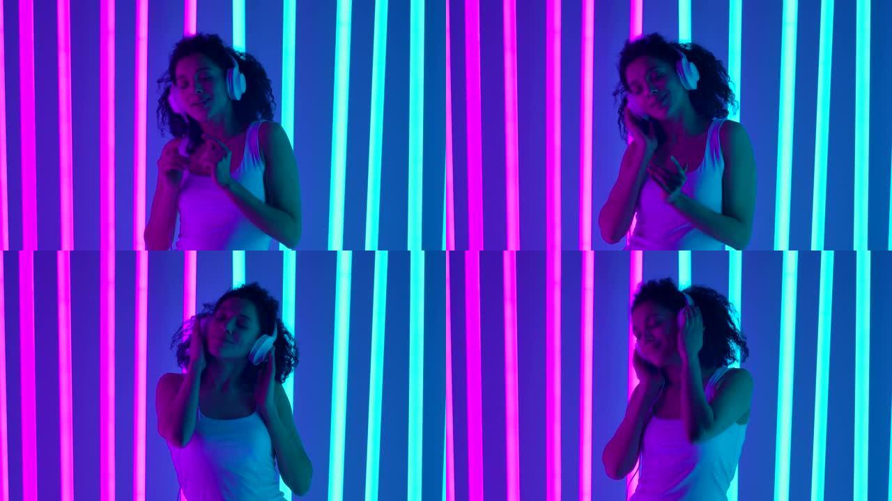 在明亮的蓝色和粉红色霓虹灯灯管照亮的工作室里，一位戴着白色大耳机的非洲裔美国妇女的肖像。女孩正在跳舞