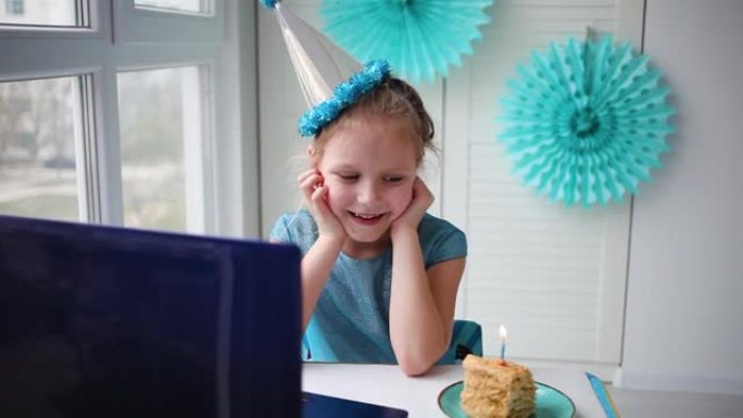 一个小女孩，在戴着帽子的笔记本电脑前弯腰大笑。通过互联网在检疫时间，自我隔离和家庭价值观，在线生日庆