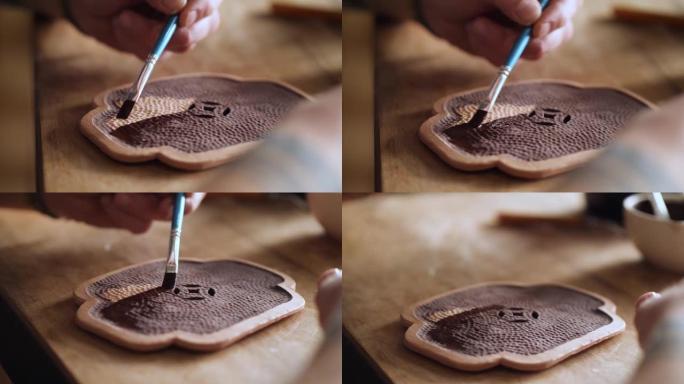 波特用刷子将釉料涂在粘土盖上。手工陶器。陶瓷餐具的制造。将釉料应用于陶瓷