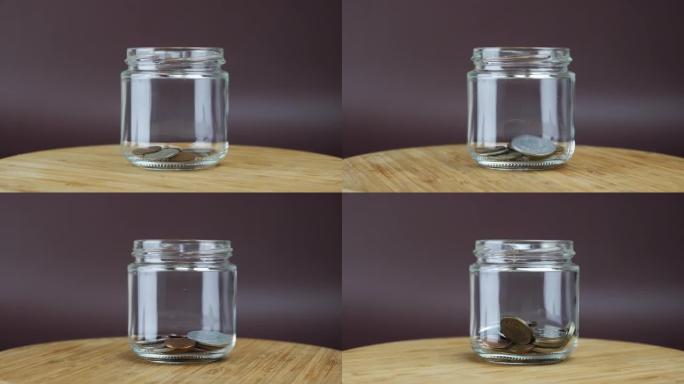 一堆硬币落在棕色背景的玻璃钱箱中，旋转镜头。人把钱币放进玻璃罐。商业和金融概念。省钱概念。