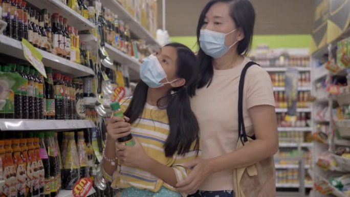 亚洲母亲和她的女儿戴着口罩，在封锁前的新型冠状病毒肺炎期间为家人囤积食物，生活方式理念。