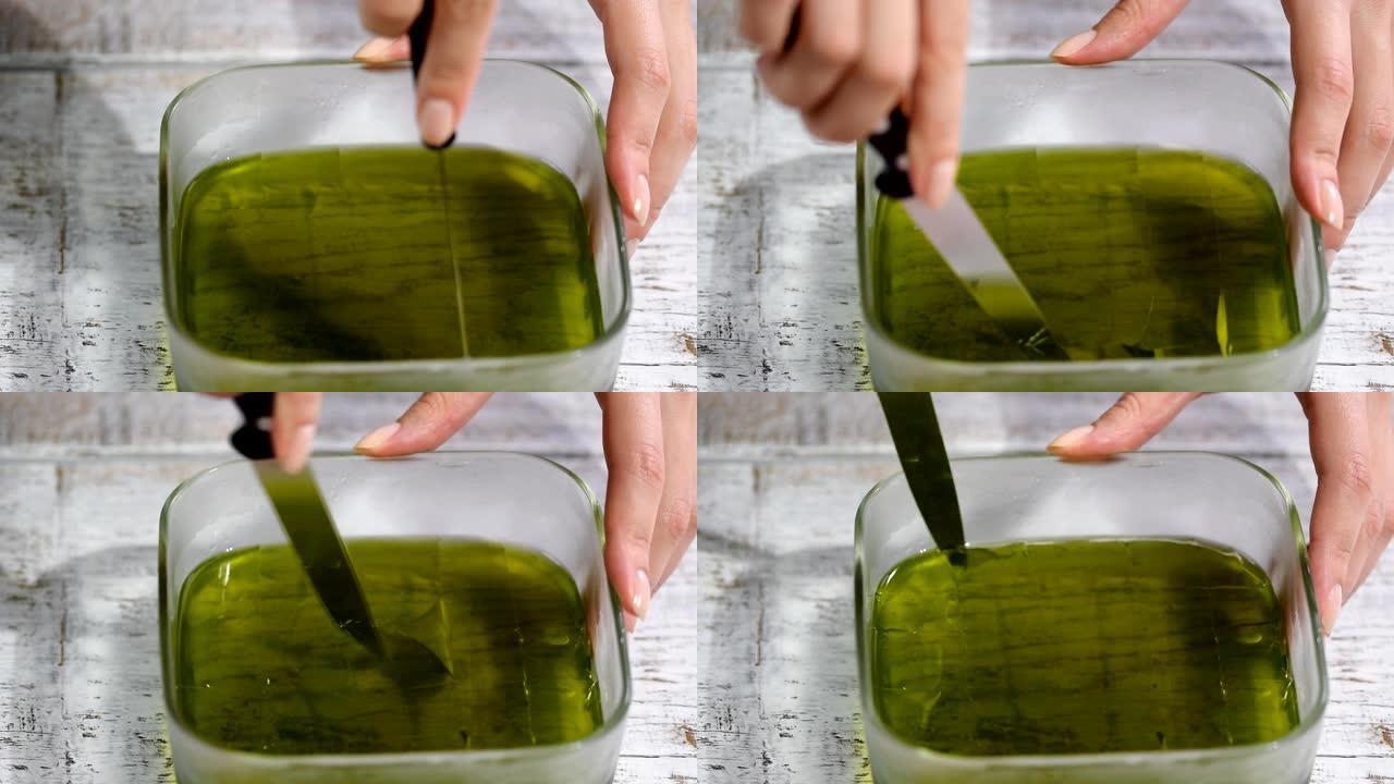 女性的手将绿色果冻切成碎片。