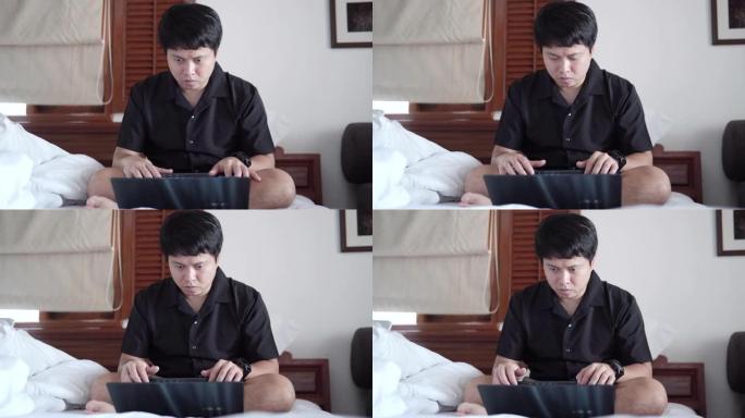 亚洲男子在家卧室工作，使用笔记本电脑。