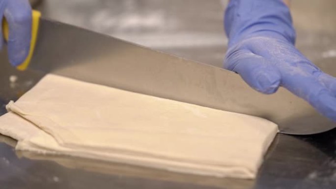 面包师手持刀并将生羊角面包面团切成三角形切片的特写镜头。在面包店工作