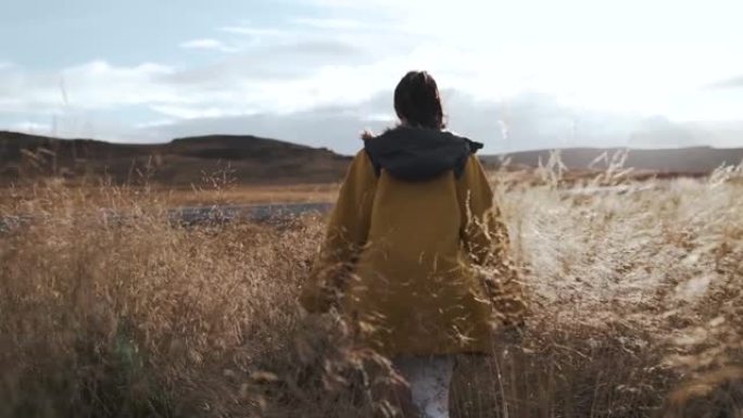 一名年轻女子走过冰岛的麦田