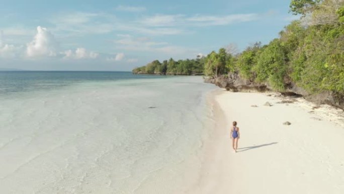 空中: 女人在热带海滩上行走，风景秀丽的绿松石水和白沙