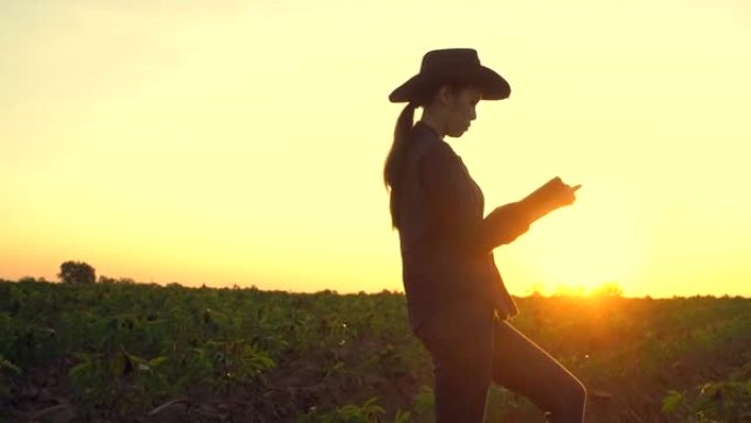 穿着胶靴的女农民带着数字平板电脑走过耕种的农田。