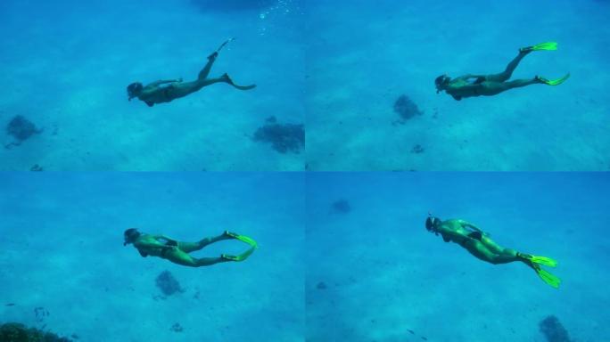 一个戴着面具和鳍的女人在沙底深处的水下游泳