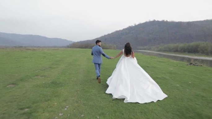 结婚夫妇在山河附近奔跑。新郎和恋爱中的新娘