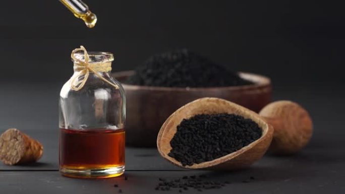 黑色孜然籽精油玻璃瓶，黑色木质背景上的黑种草，滴油