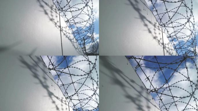 高压下带刺铁丝网的监狱混凝土墙。以不寻常的角度优雅地平移。戏剧性的视频。
