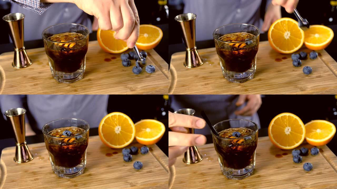 酒保将橙子和蓝莓放在带有吸管的岩石玻璃杯上的酒精鸡尾酒中。