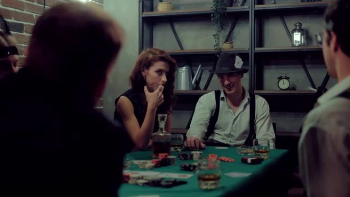 戴着帽子和背带的家伙高兴，微笑着用手指敲桌子。有钱人玩扑克。
